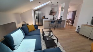 A modern living room with a sofa, coffee table, and a kitchen area in the background. - Stylish and Elegant Crikvenica Apartments (Crikvenica)