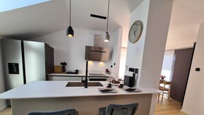 A modern kitchen with a central island, two bar stools, pendant lighting, and a clock on the wall. - Stylish and Elegant Crikvenica Apartments (Crikvenica)