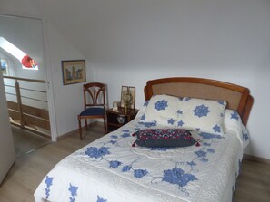Ein Schlafzimmer mit einem hölzernen Bett, einem Sessel, einem kleinen Tisch mit Lampe und einem Bild an der Wand.