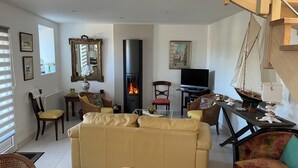 A living room with a beige sofa, a fireplace, a television, and various decorative items. - Fully renovated farmhouse in village near a typical fishing port (Hôpital-Camfrout)