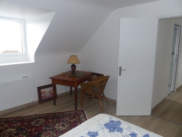 Ein Schlafzimmer mit einem Bett, einem Schreibtisch mit Lampe, einem Stuhl, einem Fenster und einer Tür.