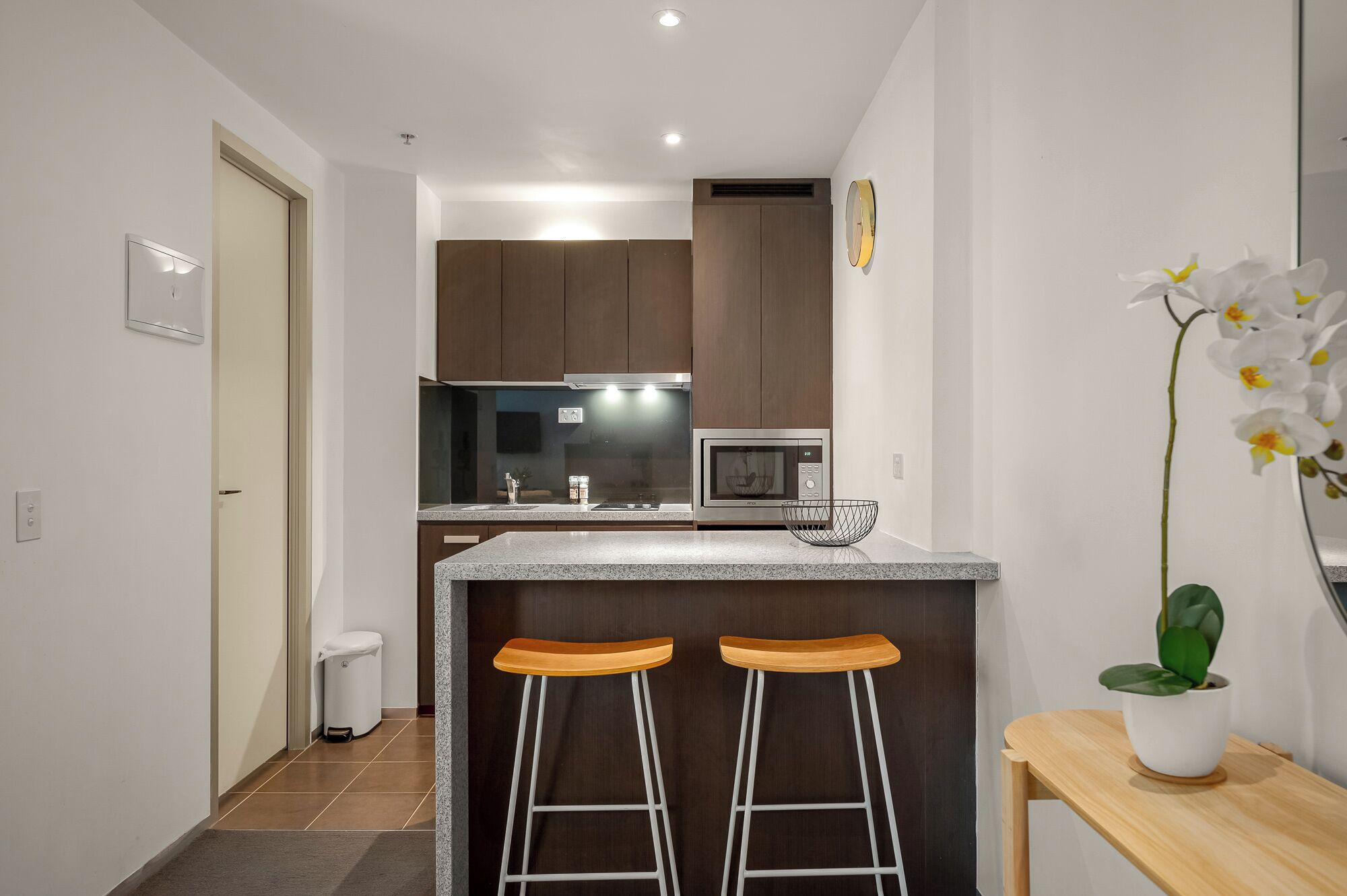 A modern kitchen with a microwave, double bar stools, and a small potted plant.