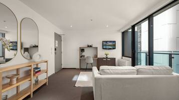 A modern hotel room with a large bed, a desk with a chair, a television, and a large window offering a view of the city.