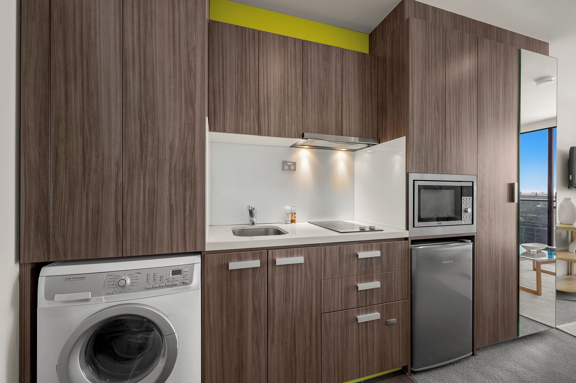 A modern kitchen with wooden cabinets, a built-in microwave, a refrigerator, and a washing machine.