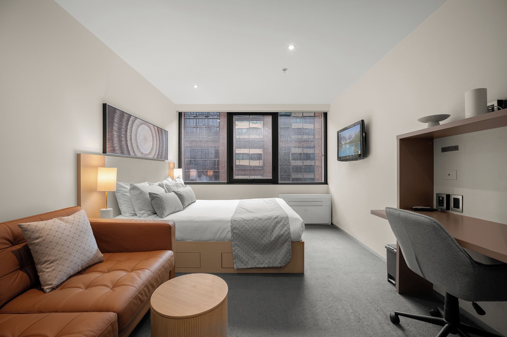 Ein modernes Hotelzimmer mit einem Bett, einer Couch, einem Schreibtisch und einem Fernseher.