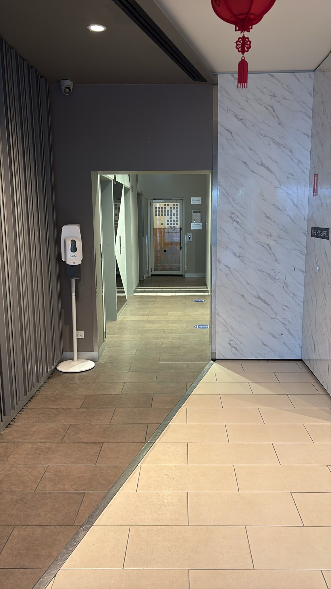 A hallway with a hand sanitizer dispenser, a security camera, and a fire safety sign.