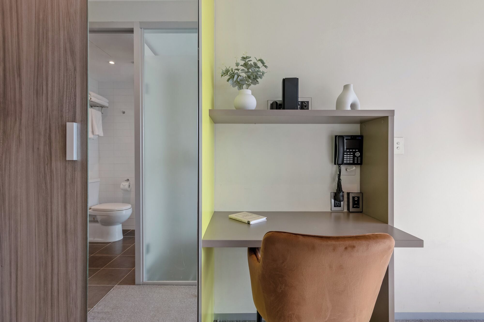 Une salle de bain moderne équipée de toilettes, d’une douche et d’une porte en verre donnant sur une chambre.