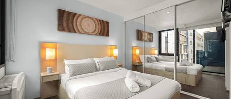 A hotel room with a large bed, two bedside tables with lamps, a large mirror, and a view of the city through the window.
