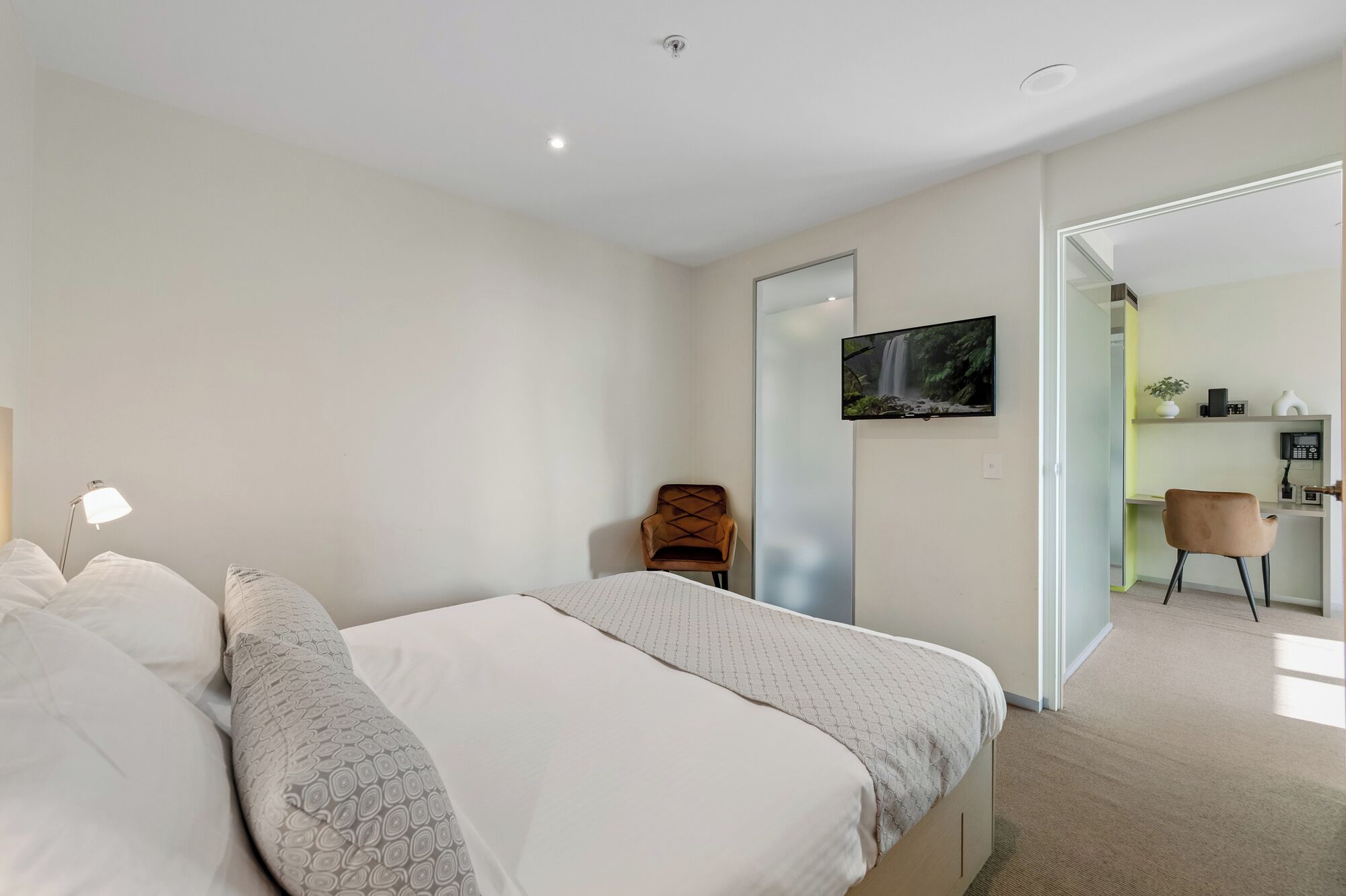 A modern bedroom with a bed, a chair, a TV, and a desk area.
