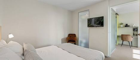 A modern bedroom with a bed, a chair, a TV, and a desk area.