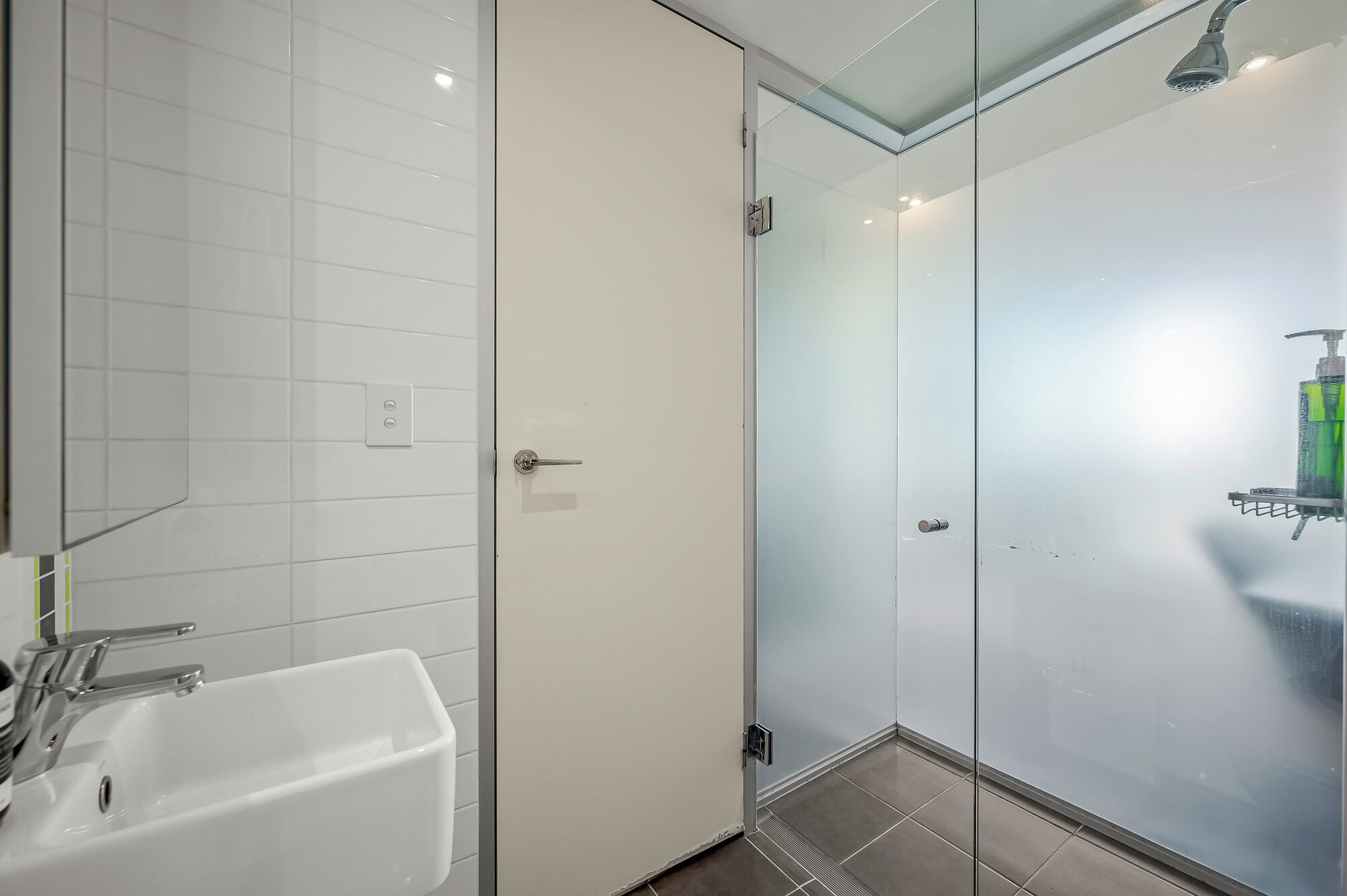 A modern bathroom with a glass shower enclosure, a white sink, and a glass door.
