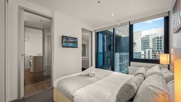 Une chambre d’hôtel moderne avec un grand lit, une vue sur la ville par une porte vitrée et une petite salle de bain équipée d’un lave-linge.