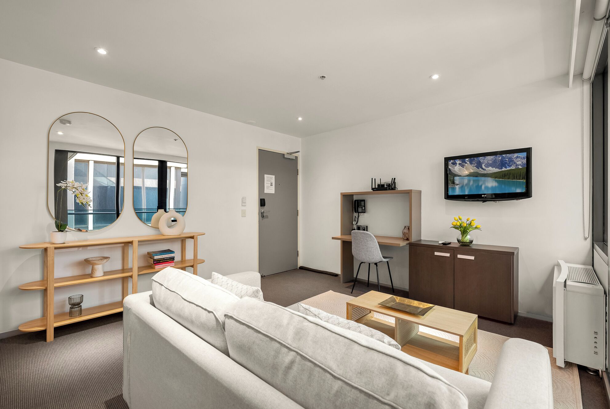 A modern living room with a sofa, coffee table, TV, and a desk with a chair.
