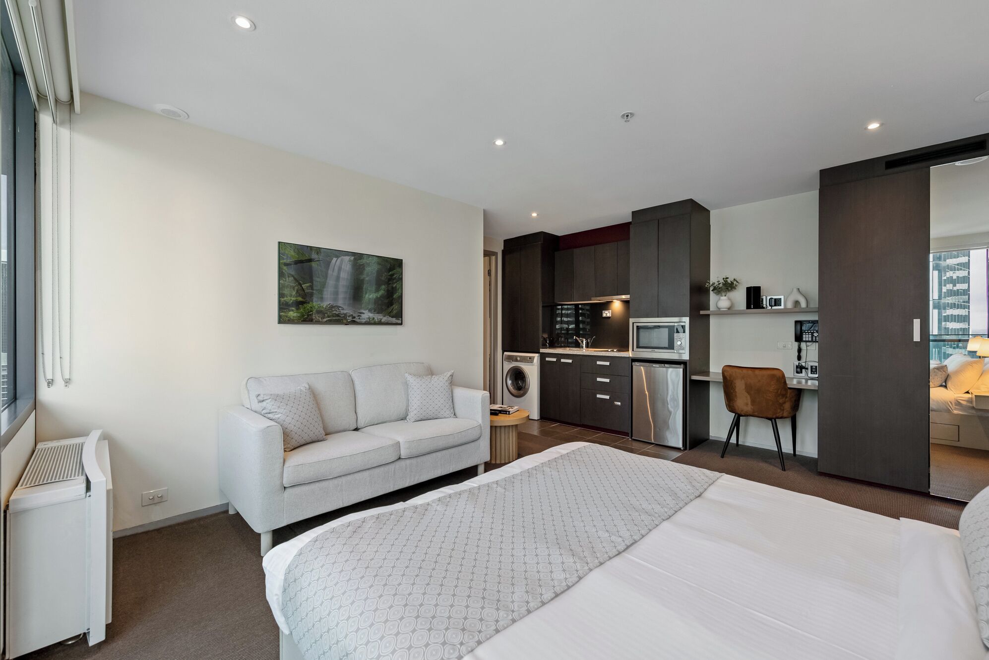 Una habitación de hotel moderna con una cama grande, un sofá, una pequeña cocina y un baño.