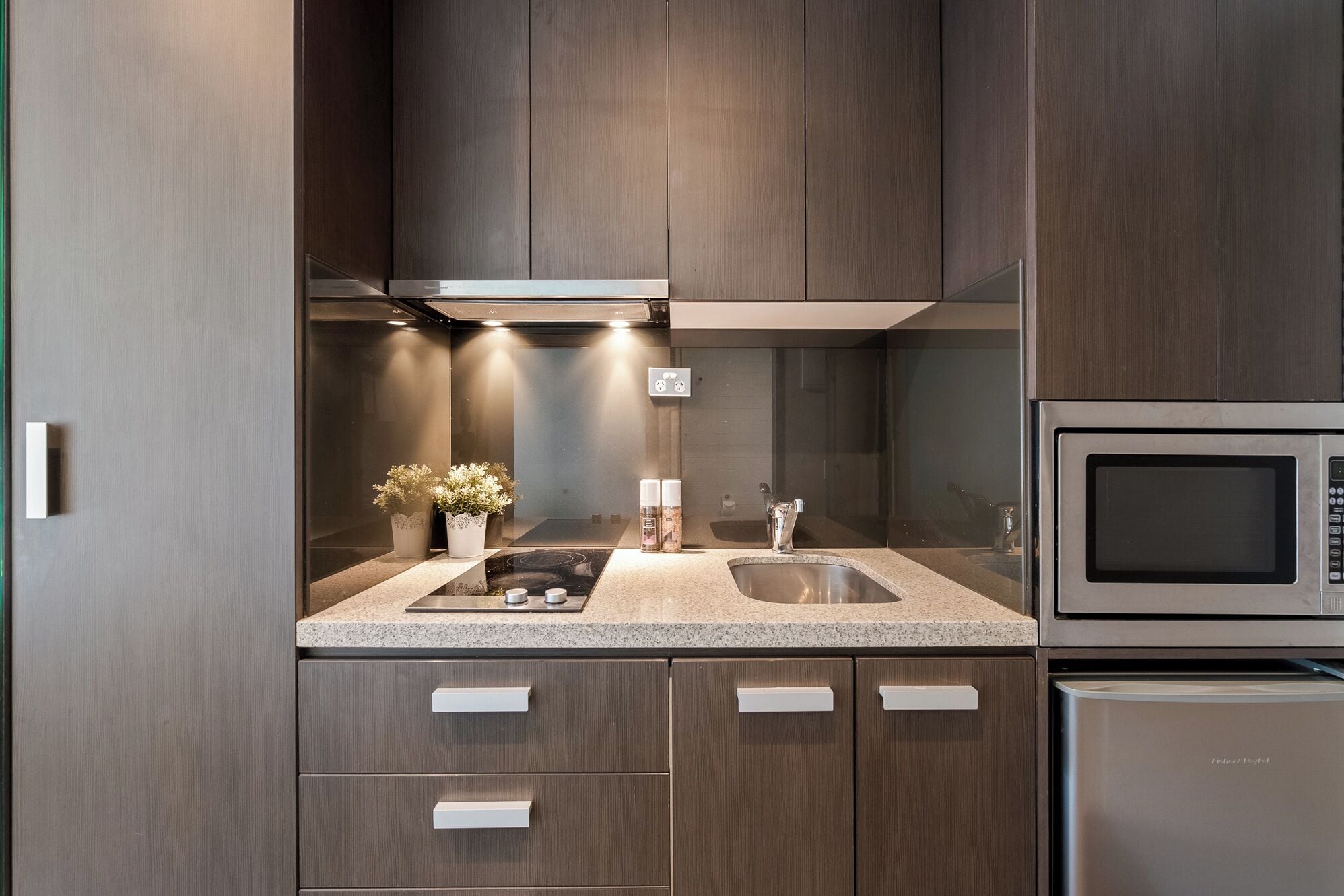 Eine moderne Küche mit dunklen Holzschränken, einer Granitarbeitsplatte, einer Edelstahlspüle, einer Mikrowelle und einem Kühlschrank.