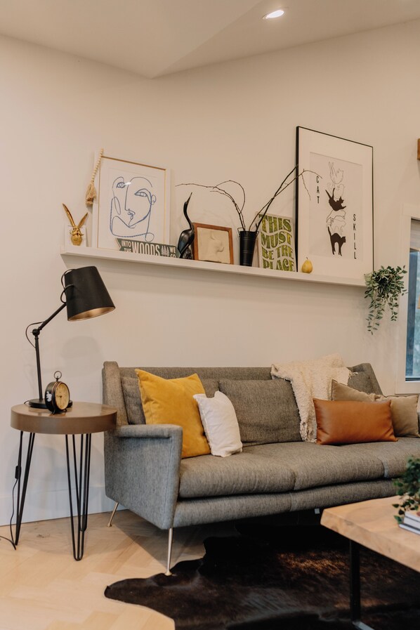 Una sala moderna con un sofá gris, una mesita auxiliar, una lámpara de pie y un estante montado en la pared con varios objetos decorativos.