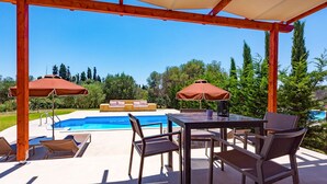 A covered outdoor area with a pool, lounge chairs, and a table with chairs. - Rhea Villa in Kefallonia (Kefalonia)