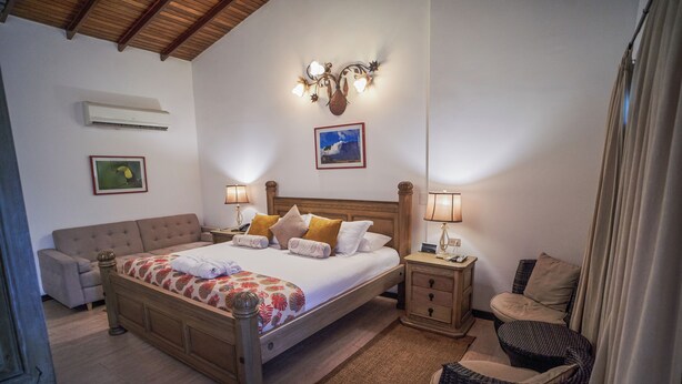 A bedroom with a wooden bed, bedside tables, a nightstand, a chair, and a wall-mounted air conditioner. - Posada Turistica Ara Meru Lodge (Gran Sabana)