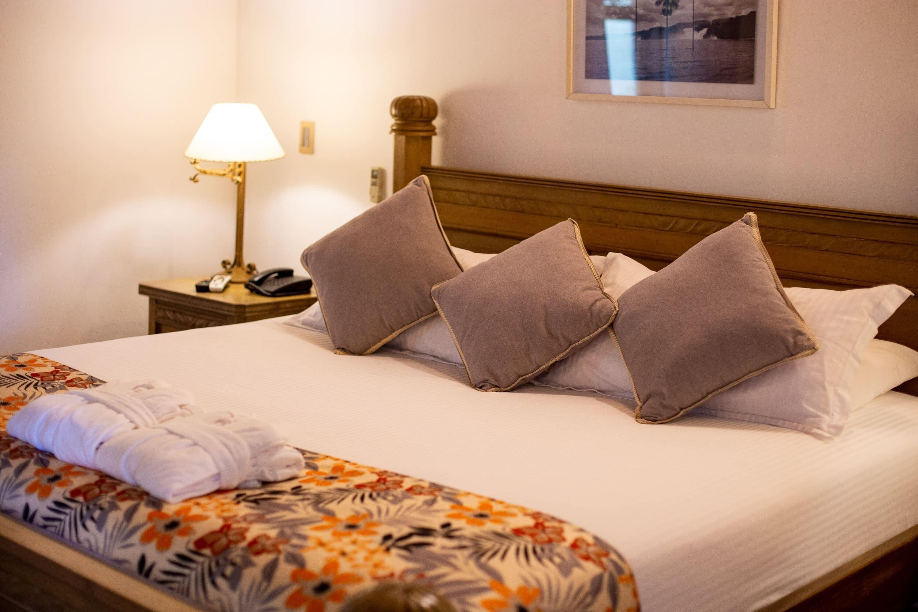 A neatly made bed with a floral bedspread, a lamp on the nightstand, and a framed picture on the wall.