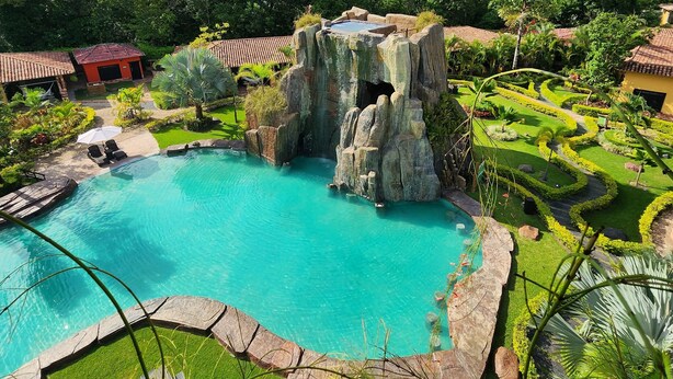 A large outdoor swimming pool with a natural rock formation, surrounded by well-maintained gardens and a few buildings. - Posada Turistica Ara Meru Lodge (Gran Sabana)