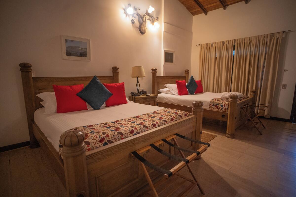 A hotel room with two wooden beds, each with a headboard, a nightstand, a lamp, and a small table.