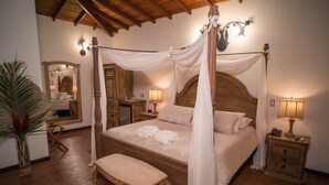 A four-poster canopy bed with a wooden headboard, bedside tables with lamps, a bench, and a large mirror. - Posada Turistica Ara Meru Lodge (Gran Sabana)