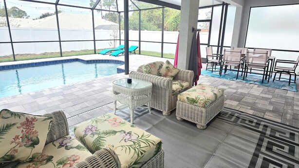 A poolside area with wicker furniture, a glass table, and a view of the pool and greenery. - Brand new house with heated salt water pool. Perfect get away in Palm Coast (Palm Coast)