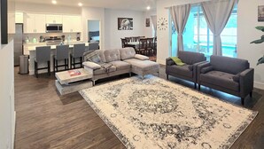 A spacious living area with a large sectional sofa, a smaller sofa, and a coffee table. There is a dining area with a table and chairs, and a kitchen in the background. - Brand new house with heated salt water pool. Perfect get away in Palm Coast (Palm Coast)
