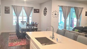 A modern kitchen with a large island, a dining area with a table and chairs, and a living area with a sofa and a TV. - Brand new house with heated salt water pool. Perfect get away in Palm Coast (Palm Coast)