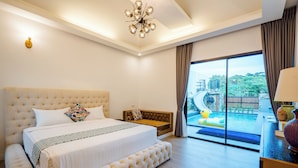 A spacious bedroom with a large bed, a sofa, and a view of a swimming pool and outdoor area.