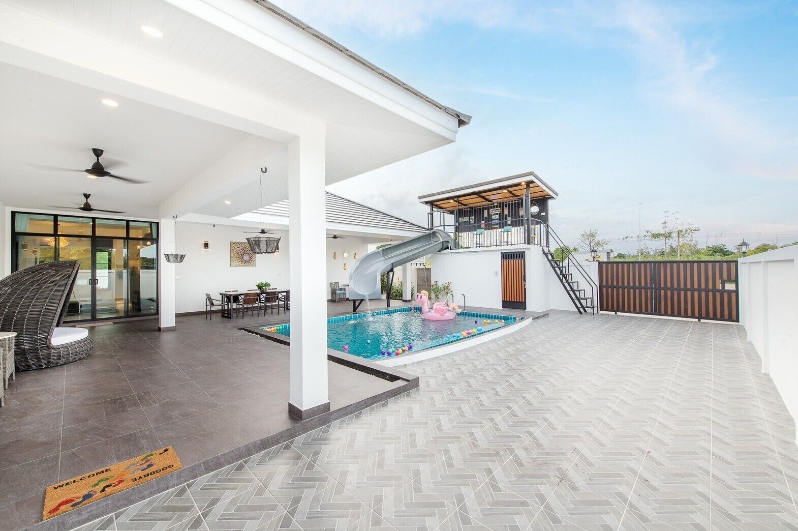 Un área de piscina exterior moderna con un tobogán, una zona de estar techada y una escalera que conduce a una terraza superior.