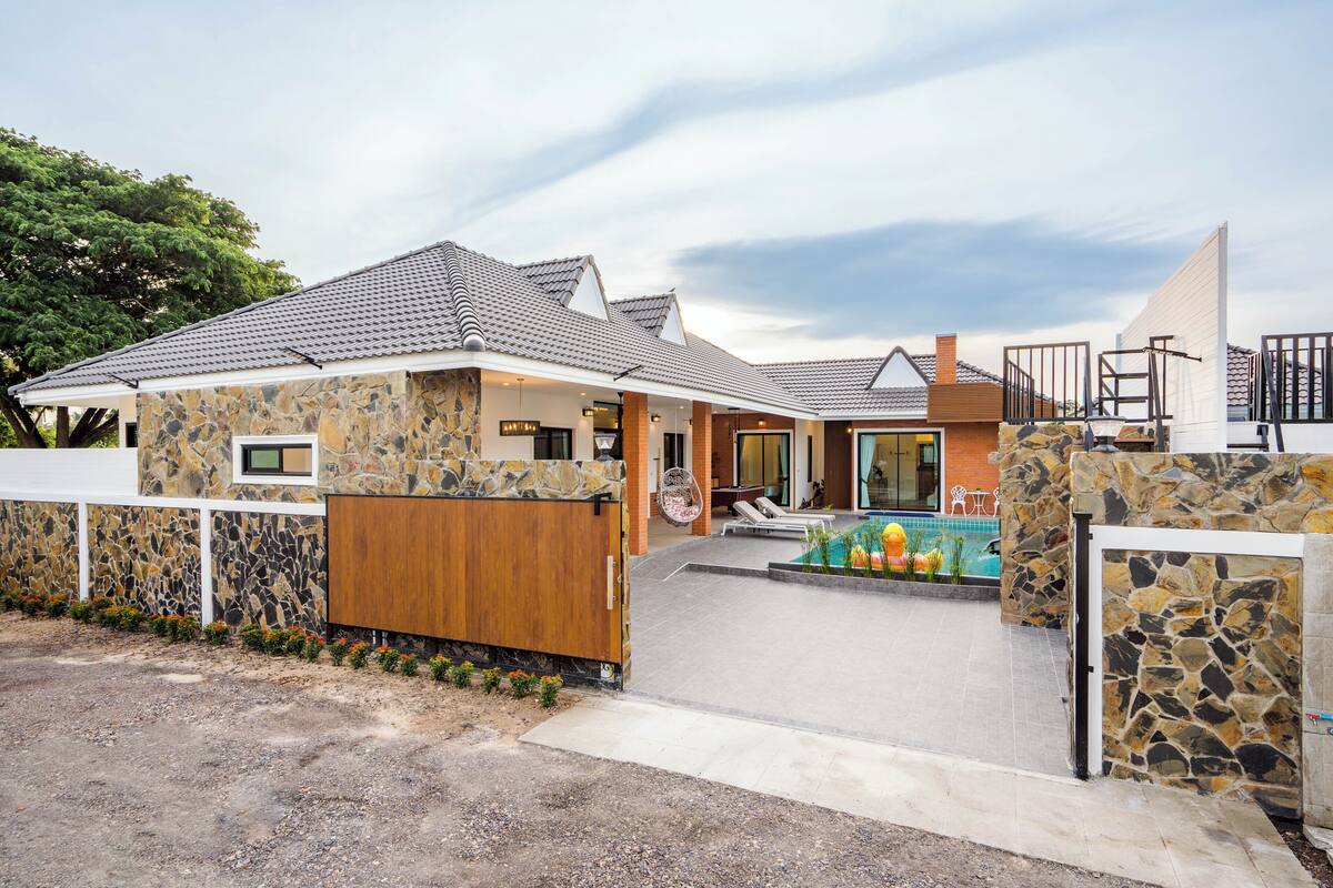 Een huis met een gevel van natuursteen, een zwembad en een overdekt terras.