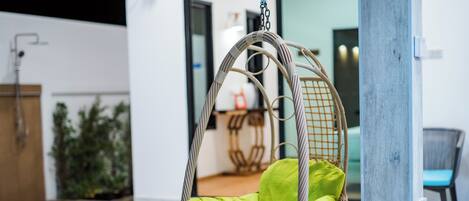 Una silla colgante de mimbre con cojines verdes en un ambiente interior moderno.
