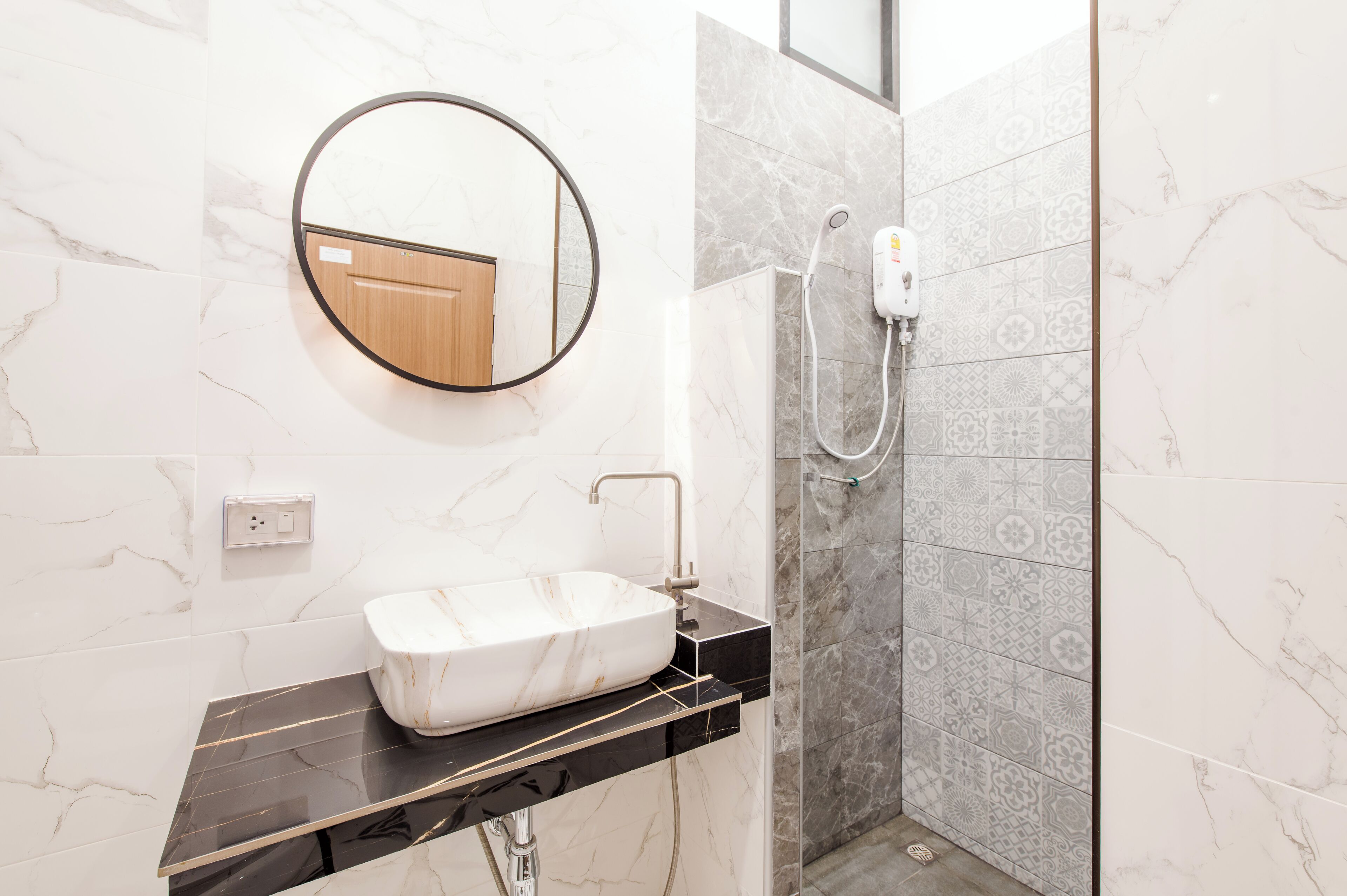 A bathroom with a marble sink, a round mirror, and a shower with patterned tiles.