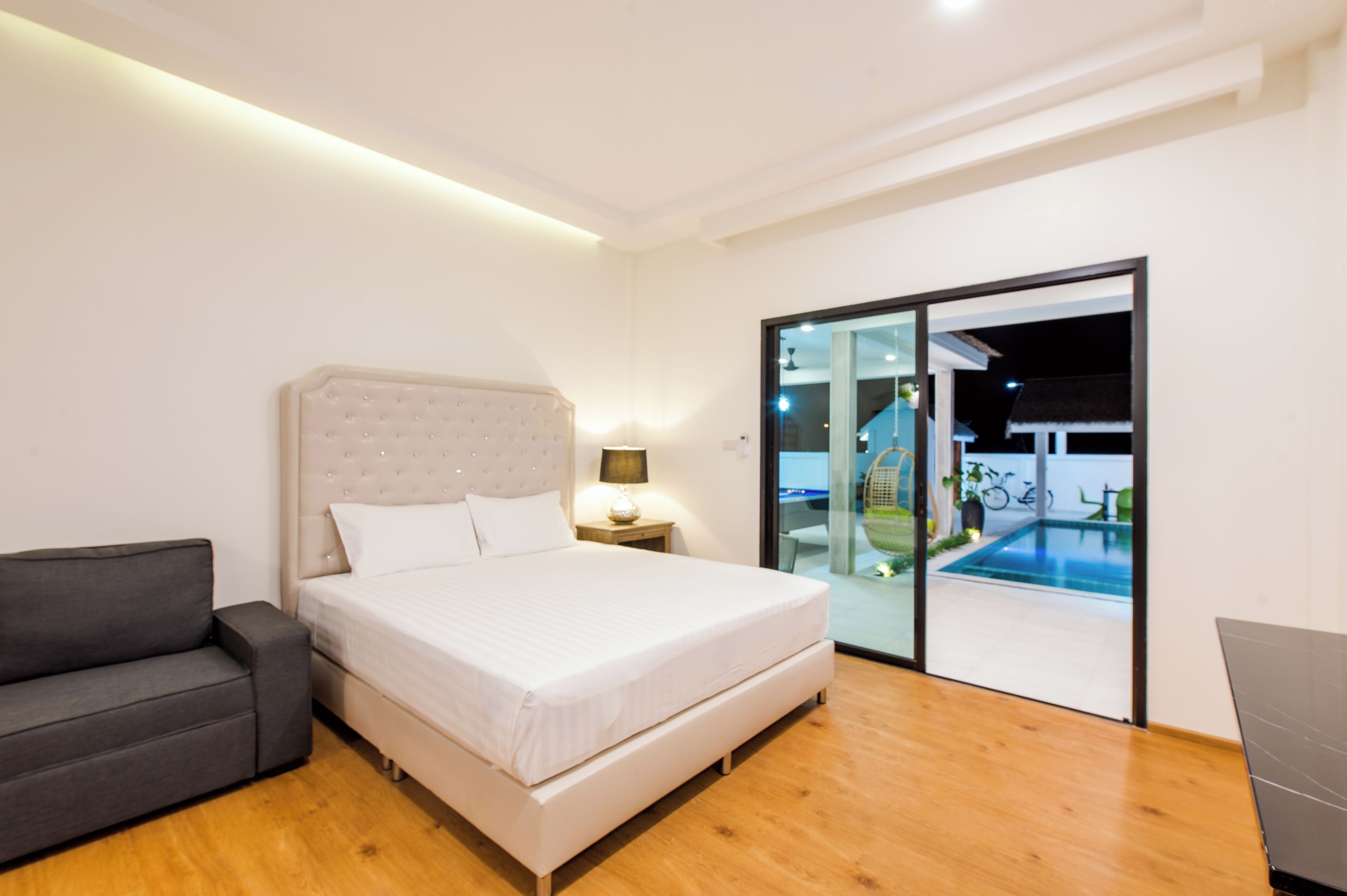 Une chambre comprenant un lit, une table de chevet, un canapé et une porte-fenêtre coulissante donnant sur un espace extérieur avec une piscine et des vélos.