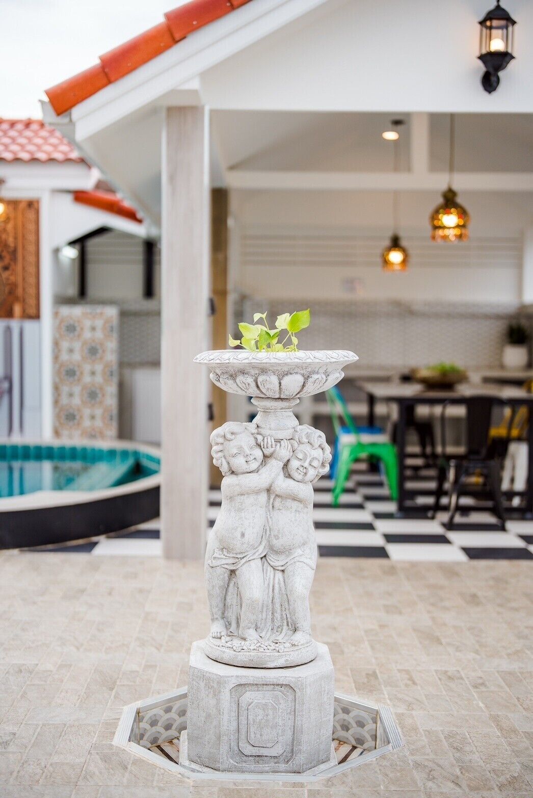 Une fontaine en pierre surmontée d’une plante, entourée d’une terrasse carrelée.