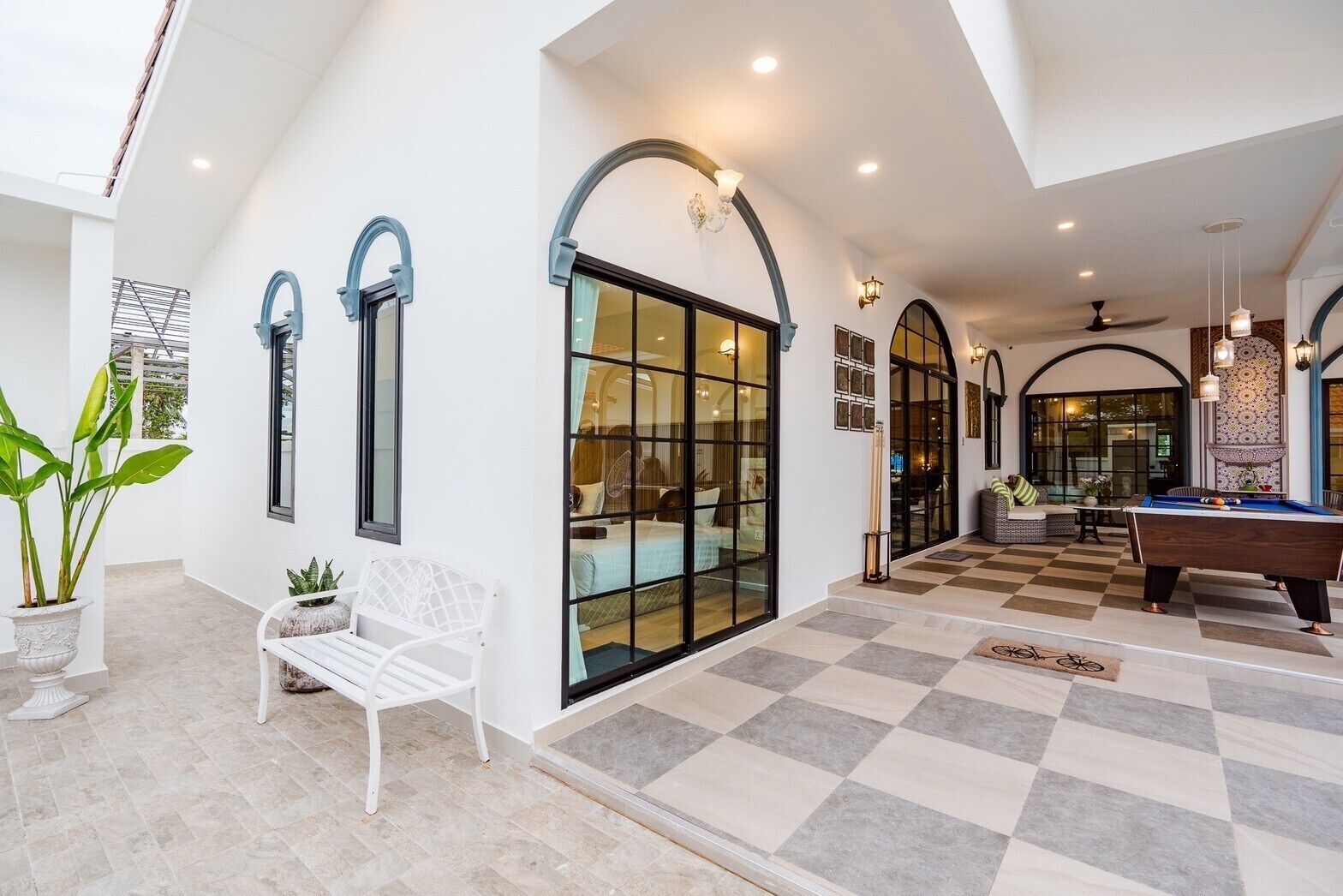 A spacious indoor area with a checkered floor, a pool table, and a seating area with a bench and potted plants.