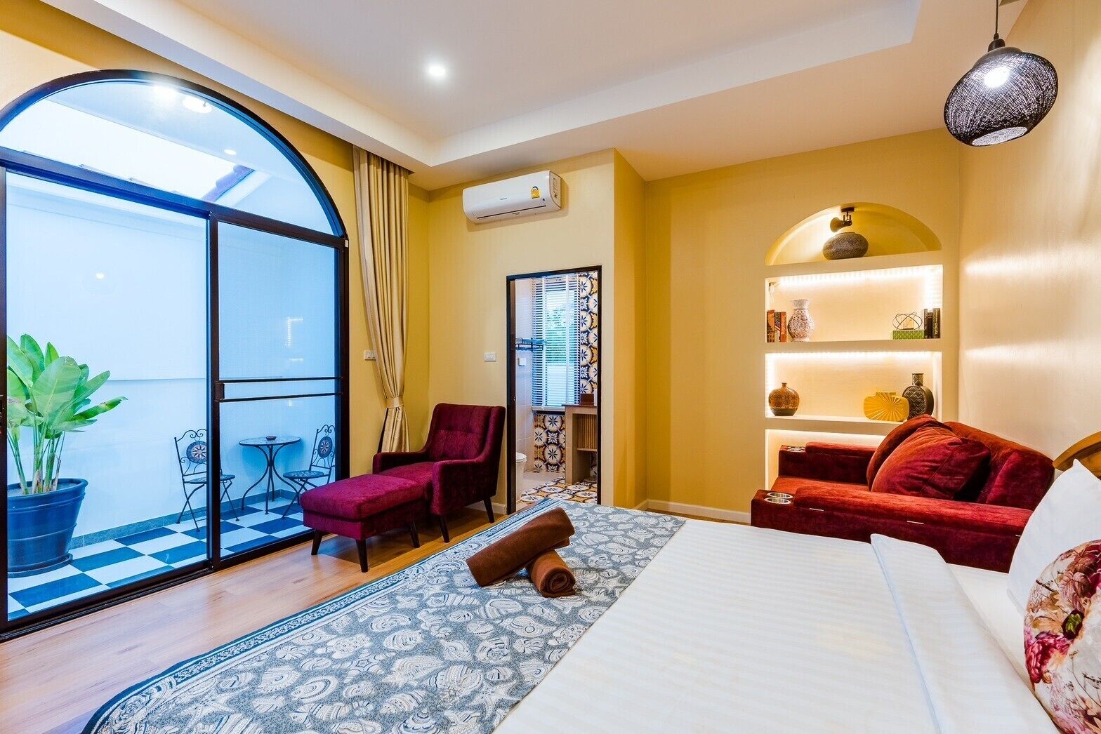 Ein Hotelzimmer mit großem Fenster, einem roten Sofa, einem Bett und einem kleinen Tisch mit Stühlen.