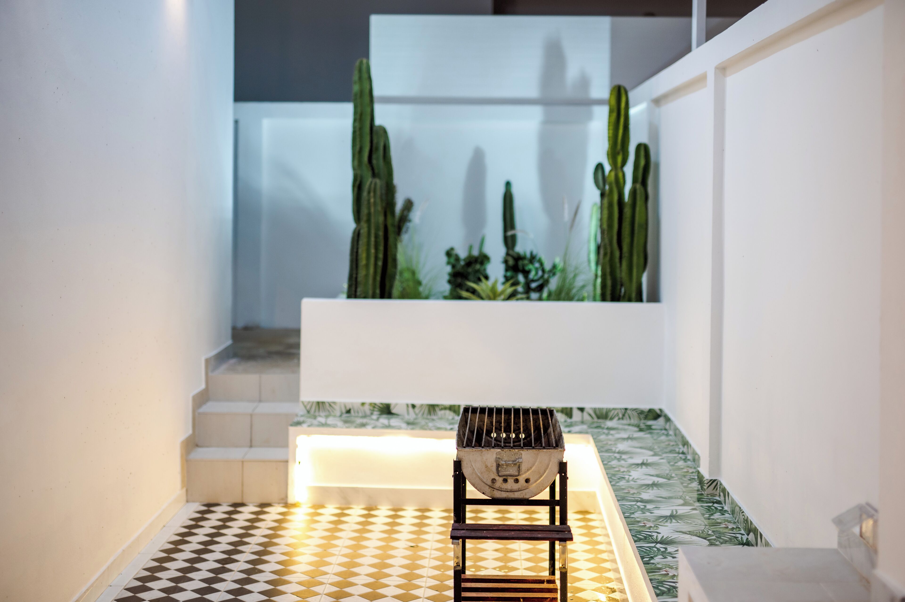 A modern interior with a checkered floor, a white bench, and a cactus garden in the background.