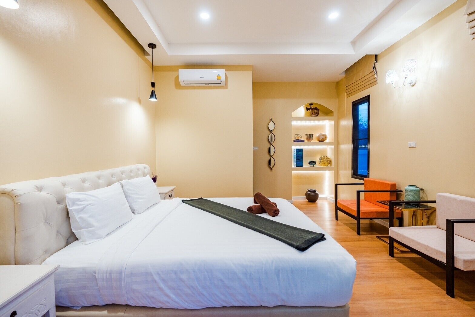 A hotel room with a large bed, a desk, a chair, a TV, and a shelf with decorative items.