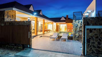 Enjoy a tranquil outdoor space with a patio, stone wall, and wooden fence, leading to a covered entrance with a glass door.