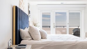A bedroom with a bed, bedside table, and a view of the outside balcony.