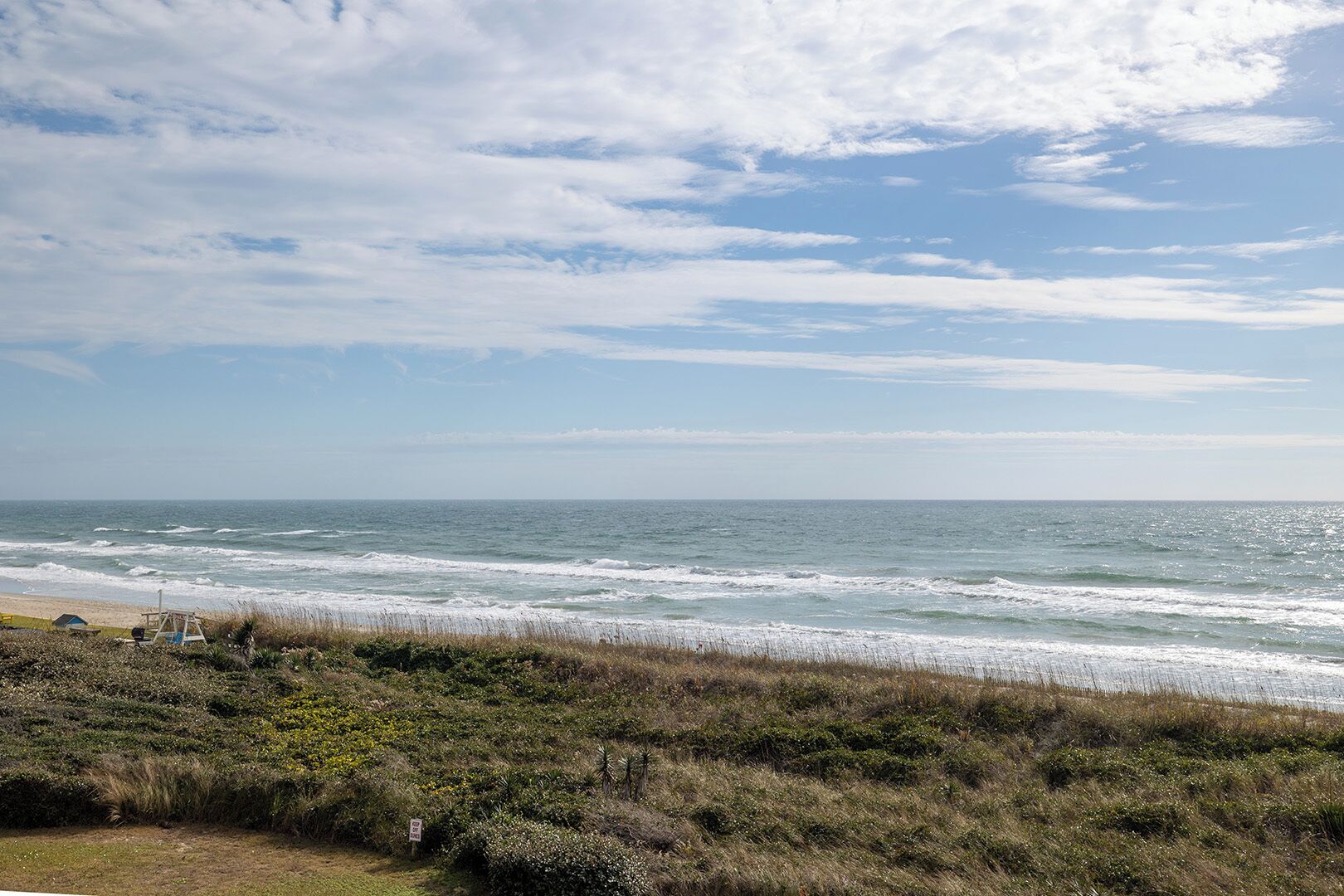 A beach with waves, a lifeguard tower, and a grassy area with bushes.