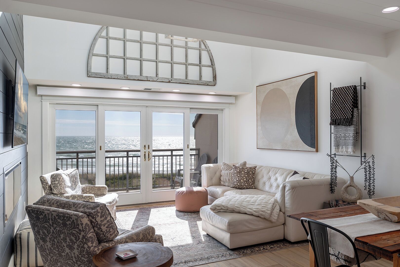 A spacious living room with a large window overlooking the ocean, a cozy seating area with a sofa and chairs, and a dining table.