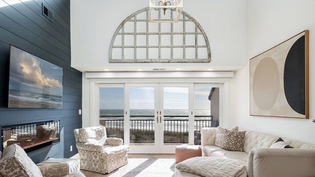 A living room with a large window overlooking the ocean, a fireplace, and a view of the beach.