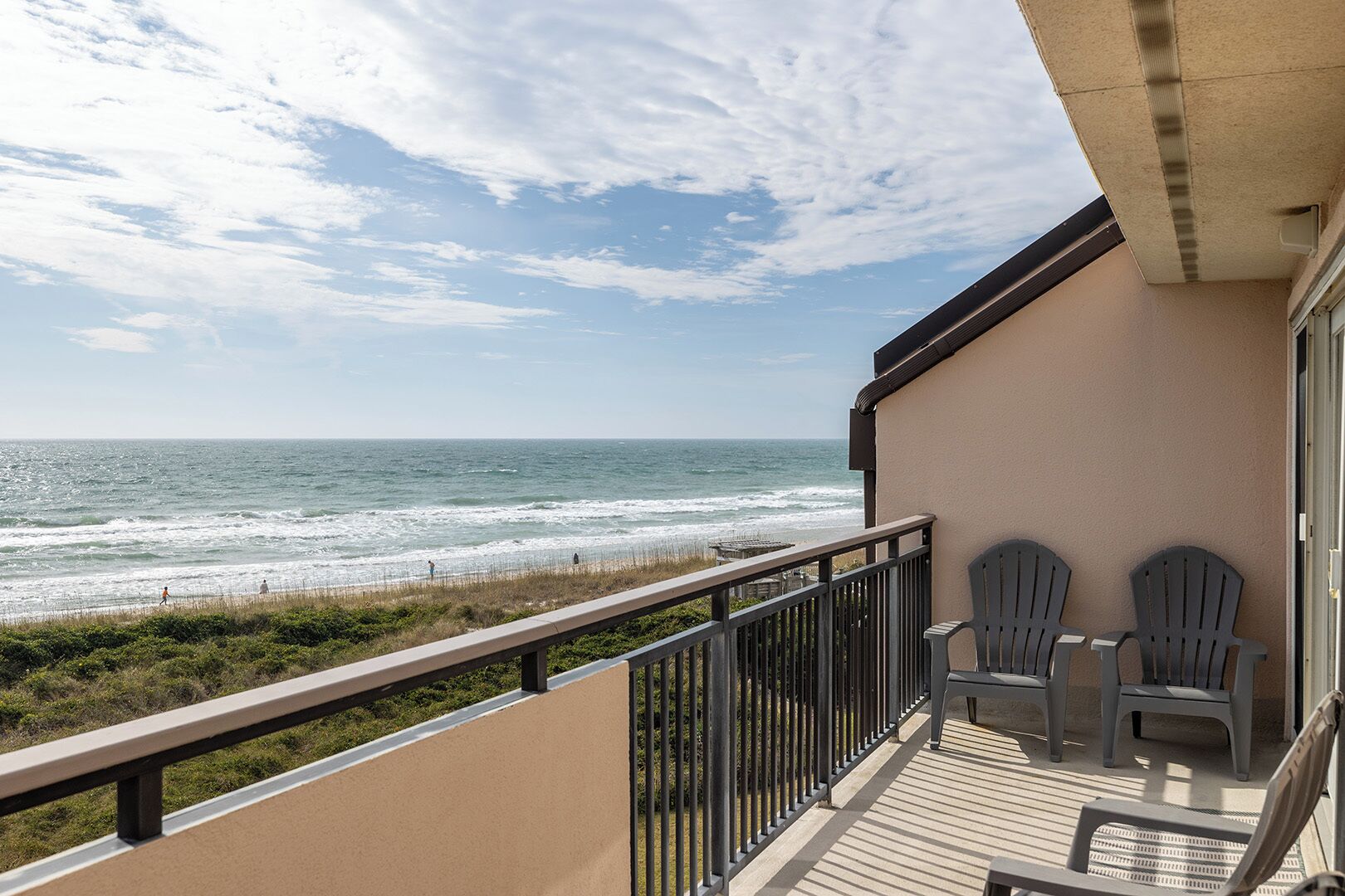 A balcony with a view of the ocean, two Adirondack chairs, and a wooden deck.