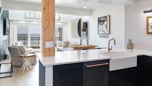 A modern kitchen with a large island, black cabinets, and a white countertop. There is a view of the ocean through a large window.