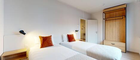 Quarto de hotel moderno com duas camas, um guarda-roupa de madeira e uma pequena mesa de cabeceira.
