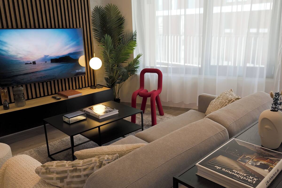 Una sala de estar moderna con televisor de pantalla plana, un sillón rojo, un sofá y una mesa de centro.