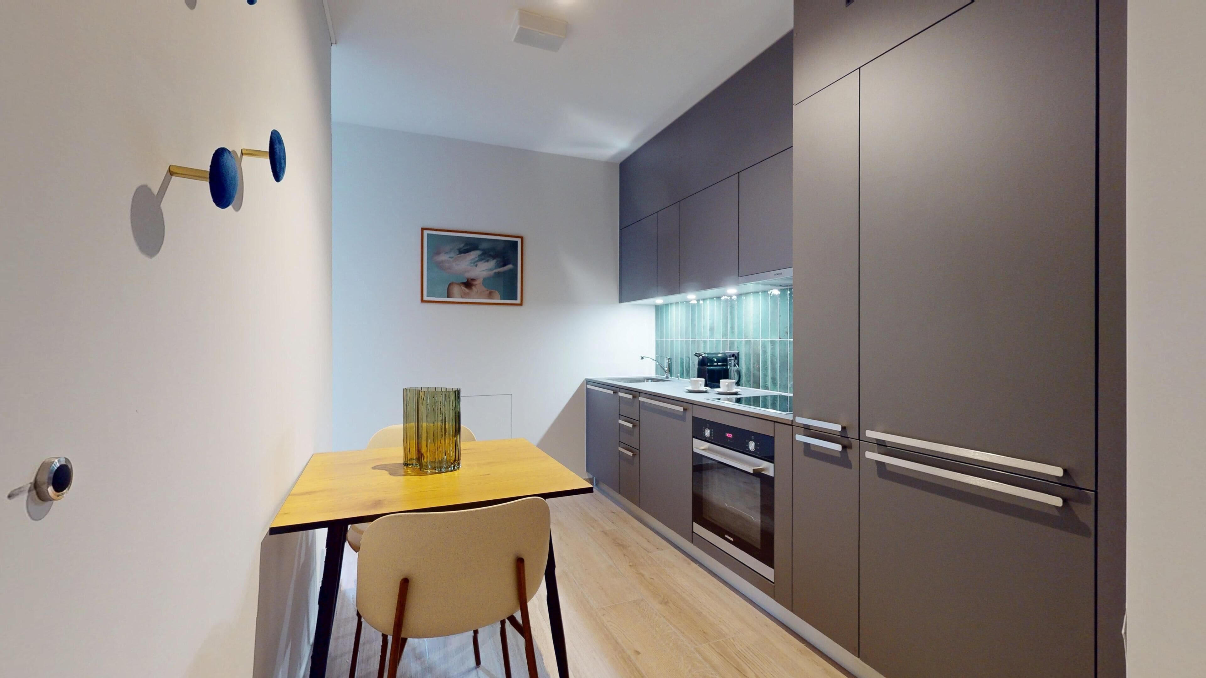 A modern kitchen with grey cabinets, a wooden table, and a chair.